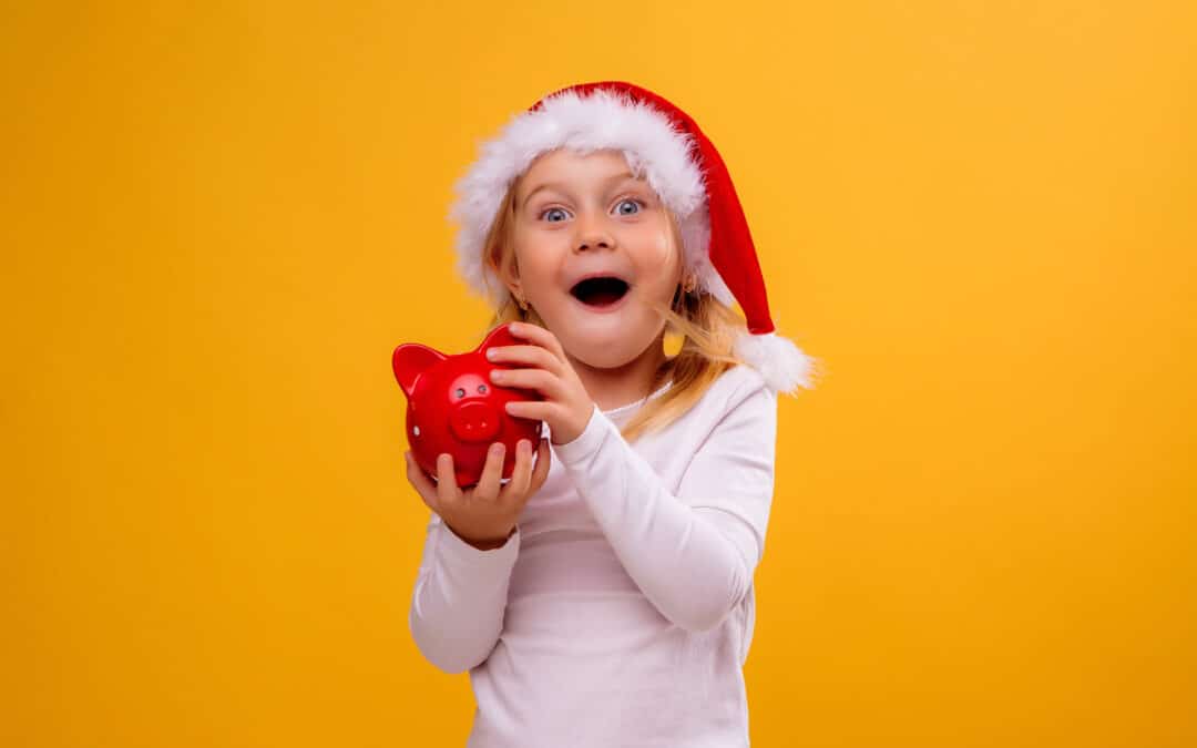 Little Blonde Girl In Santa Hat Holding Piggy Bank On Yellow Bac